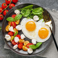 Fried eggs and Caprese salad with tomatoes, mozzarella cheese and basil leaves in a plate. Top view.