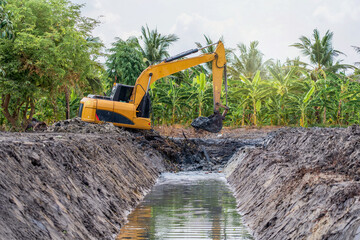 Excavator digging mud clay soil from pond bottom to expand and lift trench with level area for...