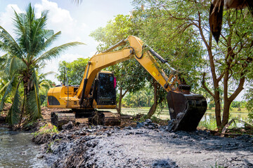 Excavator digging mud clay soil from pond bottom to expand and lift trench with level area for...