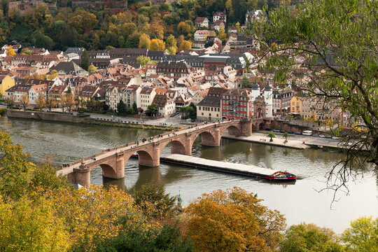 autumn view from the Philosophenweg walking trail towards the historical city Heidelberg with the famous Karl Theodor Bridge (German: Karl-Theodor-Br&uuml;cke) and the old gate. Pedestrians on the bridge.