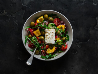 Traditional Greek salad with fresh vegetables, arugula and feta cheese on a dark background, top...