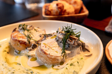 Fish cutlets, meatballs, salmon hamburger steak garnished with fresh dill, served with creamy mushroom sauce and sides in a restaurant setting. Fine eating