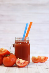 Delicious tomato juice in a glass and fresh tomatoes on a light gray table. Tomato juice on a light background. Fresh juice in a glass with a handle. Glass with juice and a straw. Vegetable drink