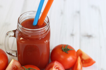 Delicious tomato juice in a glass and fresh tomatoes on a light gray table. Tomato juice on a light background. Fresh juice in a glass with a handle. Glass with juice and a straw. Vegetable drink