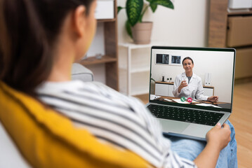 A young woman in a home environment attentively listens to a doctor on a telehealth video call on...