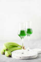 Green banana liqueur in grappas glasses and fresh  bananas on the table. Copy space