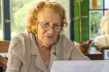 Elderly woman reading documents at home with a concentrated expression