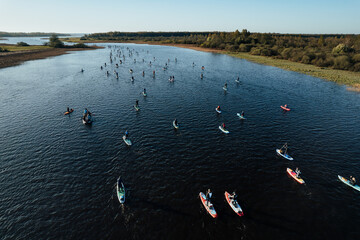 An aerial shot captures a vibrant scene of numerous SUP paddleboarders enjoying a sunny day on a...
