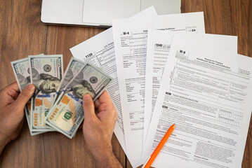 Plakat Man freelancer holds cash counting dollar banknotes preparing money for future tax obligations in compliance with law sitting at workplace with tax forms and laptop