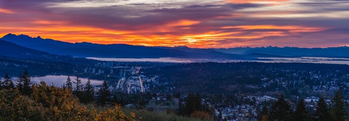 Aerial panoramic view of Fraser Valley, BC, Canada, with dramatic sunrise over mountains in silhouette on horizon.