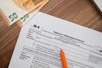 Obraz premium Pen rests on W-4 tax form flanked by euro bills and laptop on office table awaiting worker input to guide employer on federal tax withholdings according to law