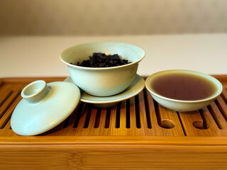 Cup or tea glass hot brew and dried tea leaves on a wooden plate, placed on a wooden table, on a white background. Brewing Chinese tea in ceramic gaiwan during the tea ceremony. 
