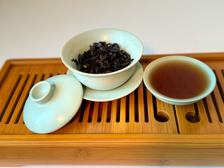 Cup or tea glass hot brew and dried tea leaves on a wooden plate, placed on a wooden table, on a white background. Brewing Chinese tea in ceramic gaiwan during the tea ceremony. 