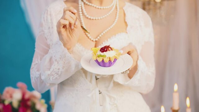 close-up female hand holding a saucer with cake basket with cream cherry on top, sweet confectionery, woman queen vintage dress medieval style classic room, blue wall pink white flowers vases candles