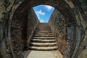 Stone staircase under archway in Galle Fort leading to blue sky and fortress wall