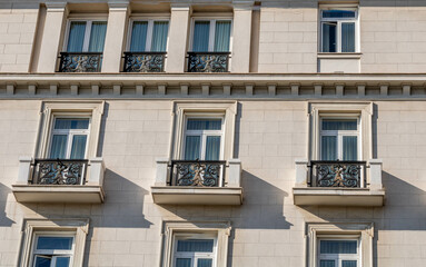 A classic building facade with three ornate balconies and large windows, showcasing elegant architectural details in neutral tones under natural light