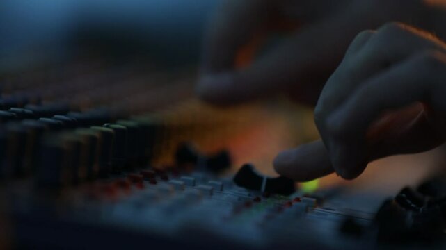 Close-up of sound technician adjusting levels on audio mixing console. Red light, sound check at the nightclub. Modern audio system.