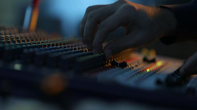 Close-up of sound technician adjusting levels on audio mixing console. Red light, sound check at the nightclub. Modern audio system.