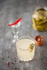 Pickle juice or brine in a glass and jar of pickled cucumbers on a gray background.