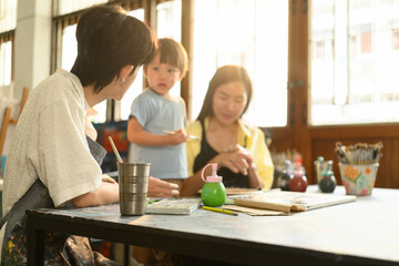 A young teacher engages with a child and his mother during a painting class in a warm, sunlit art studio