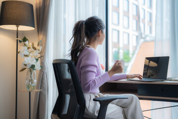 Young Asian businesswoman is working from home, sitting on an ergonomic chair in front of her...