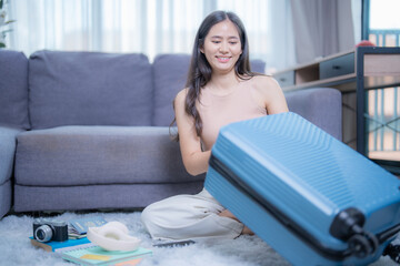 Happy tourist preparing luggage for travel vacation, smiling asian girl packing clothes into suitcase on floor in living room, traveler woman planning holiday trip with passport and camera