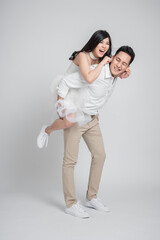Happy Asian groom gives a bride piggyback ride on white background having fun together