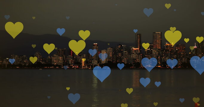 Image of yellow and blue hearts floating over night cityscape - Powered by Adobe