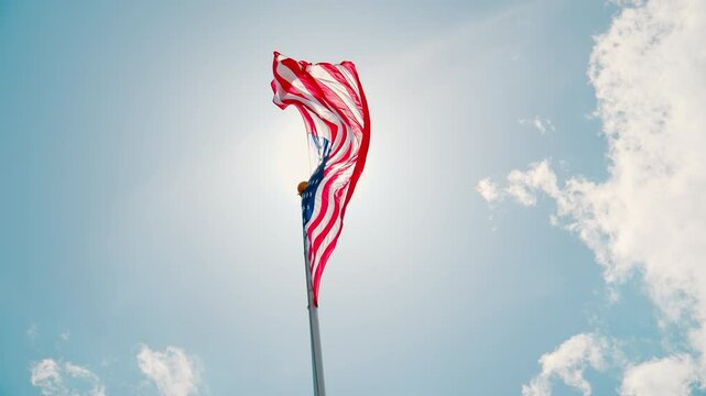 USA flag waiving on the flagpole with a background of the clear blue sky and white cloud.