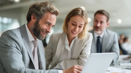 Three successful business professionals engage in a collaborative meeting while analyzing data on a laptop in a modern office environment
