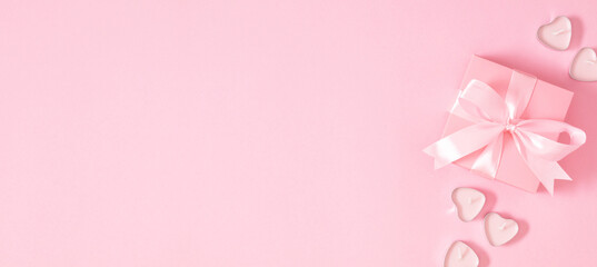 On a pink background a beautiful pink gift box with a satin ribbon and heart-shaped candles. Valentine's Day, Mother's Day, Birthday, Wedding. Top view. Banner. © prime1001