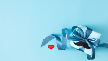 Happy Father's Day concept. Top view of beautiful gift boxfor Father's Day holiday, red heart, decorative mustache on blue background. Banner.