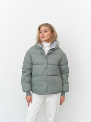 Stylish woman poses in a chic studio with a modern puffer jacket and white pants