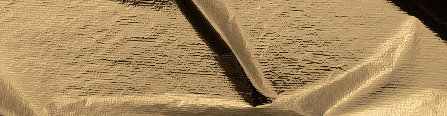 Gold foil crumpled texture with a shiny, metallic surface. Abstract, reflective pattern with folds