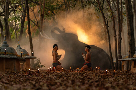 Muay Thai Fighters Performing Wai Kru Ritual in Forest with Elephant. Traditional Martial Arts Ceremony at Sunset Surrounded by Candles.