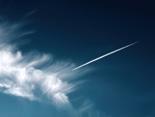 Bright blue sky with wispy clouds and high altitude jet trail creating streak across sky, evoking sense of movement