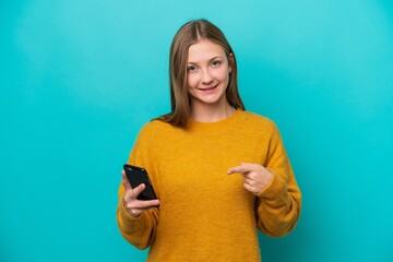 Young Russian woman isolated on blue background using mobile phone and pointing it
