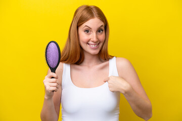 Young redhead woman holding a hairbrush isolated on white background with surprise facial expression