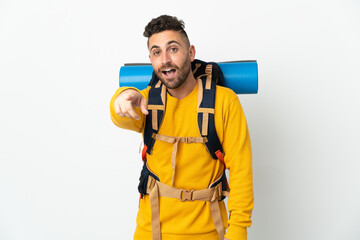 Young mountaineer man with a big backpack over isolated background surprised and pointing front