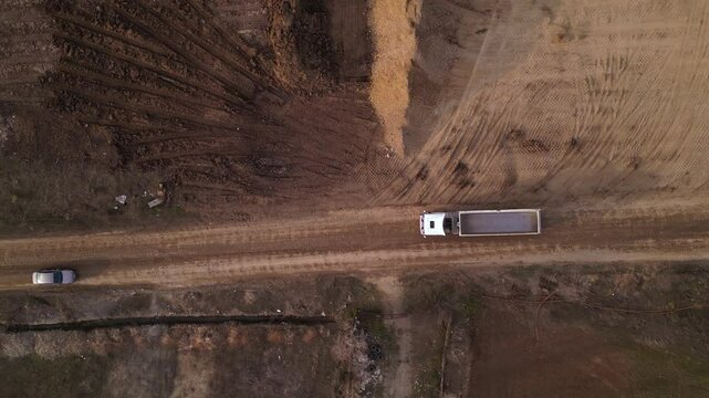 Aerial high angle footage of end dump truck unloading dirt and gravel at a dump site during the construction of a highway.  Top down drone view of  dumping payload after hauling from industrial site.
