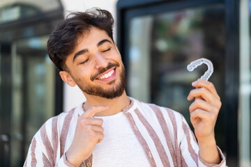Handsome Arab man at outdoors holding invisible braces with happy expression