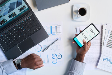 From above view of unrecognizable male hands using online calculator app on smartphone at workplace in office