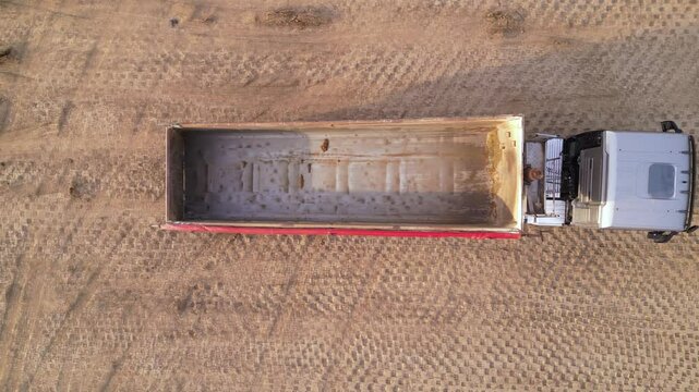 Aerial high angle footage of end dump truck unloading dirt and gravel at a dump site during the construction of a highway.  Top down drone view of  dumping payload after hauling from industrial site.
