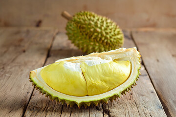 Durian Delight: A single slice of ripe durian fruit, with its creamy yellow flesh, sits alongside a whole durian with its spiky green exterior, on a rustic wooden surface. Ai generative