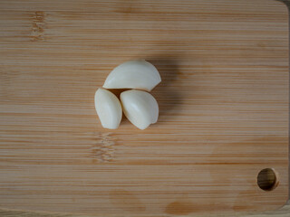 Three peeled garlic cloves on a wooden cutting board, top view of fresh ingredients for cooking or recipe preparation.