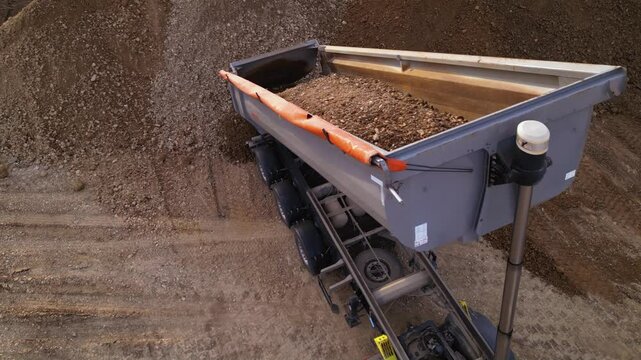Aerial high angle footage of end dump truck unloading dirt and gravel at a dump site during the construction of a highway.  Top down drone view of  dumping payload after hauling from industrial site.
