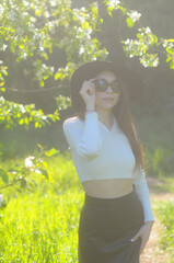 young girl walking in a summer park in a black hat in a white blouse and skirt
