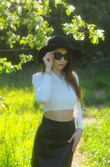 young girl walking in a summer park in a black hat in a white blouse and skirt
