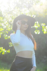young girl walking in a summer park in a black hat in a white blouse and skirt