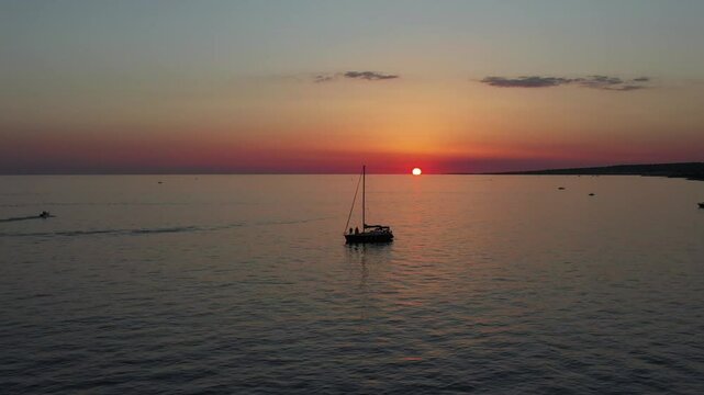 Aerial view of an orange sunset with boats at anchor in a bay of Salento. Sailboats moored in a calm bay with golden sky over the sea. Puglia, Marina di San Gregorio, Lecce, Italy